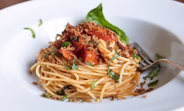 Assiette de spaghettis garnis de sauce tomate fraîche, herbes hachées et une feuille de basilic avec une fourchette posée sur le côté.