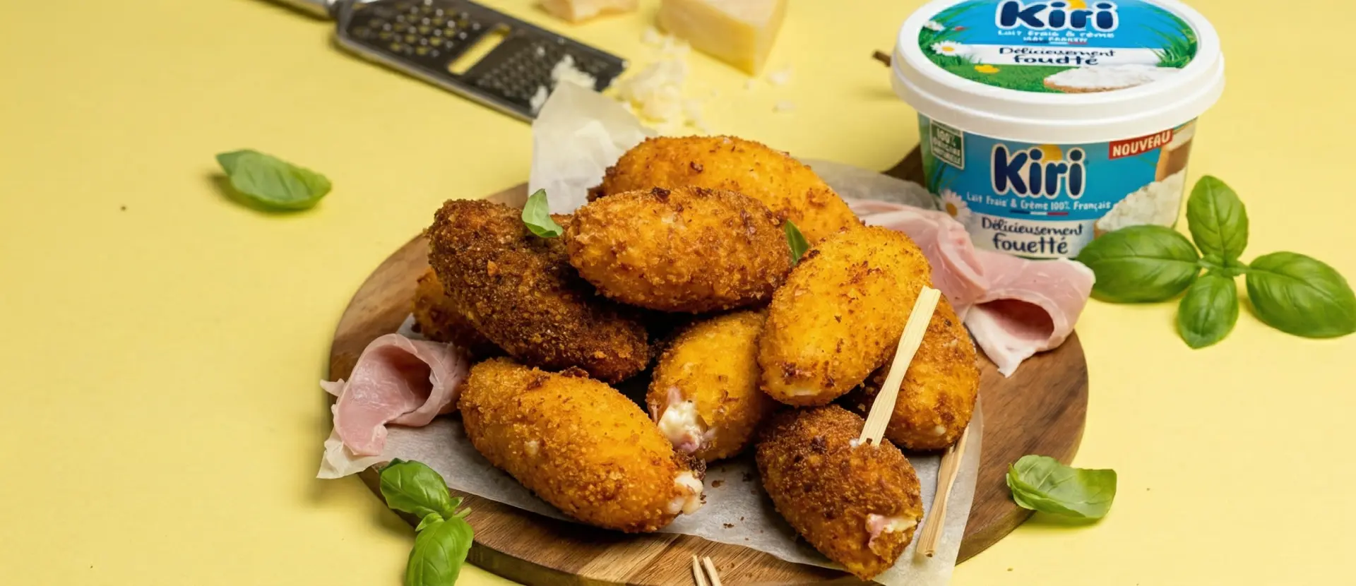 Croquettes dorées croustillantes garnies de fromage fondu, servies avec du jambon et du fromage Kiri fouetté sur planche en bois.