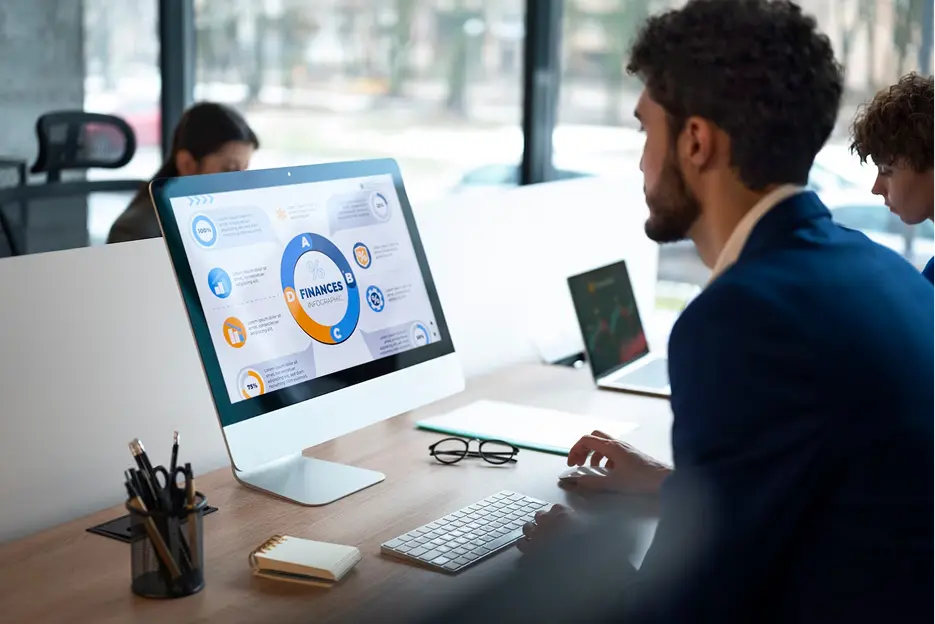 Man in blue suit working on a computer displaying a colorful finance infographic in a modern office.