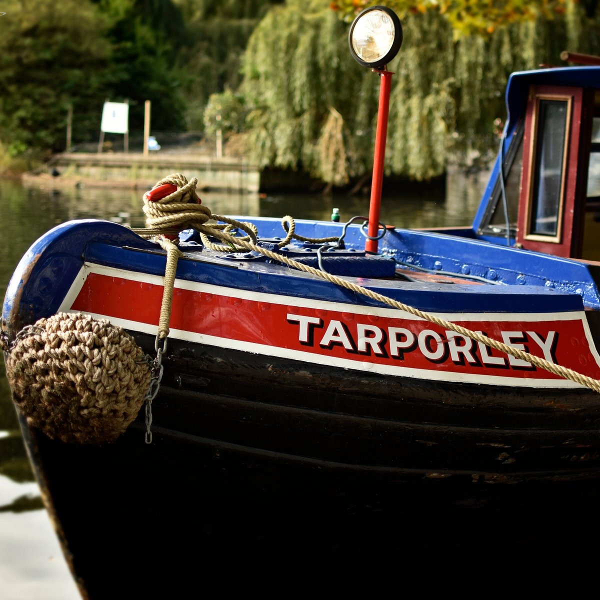 The bow of the historic narrowboat Tarporley, painted blue, red and black with its name in white lettering, moored on the canal