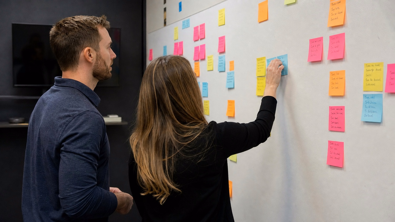 STICKY NOTE WALL An IT professional two people standing at a wall covered wi