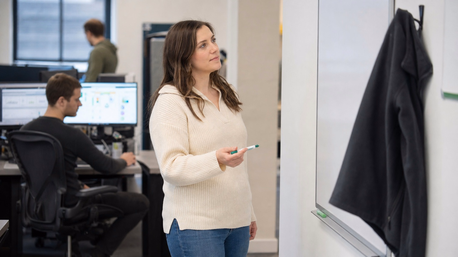 Woman with marker at blank whiteboard, fleece jacket nearby