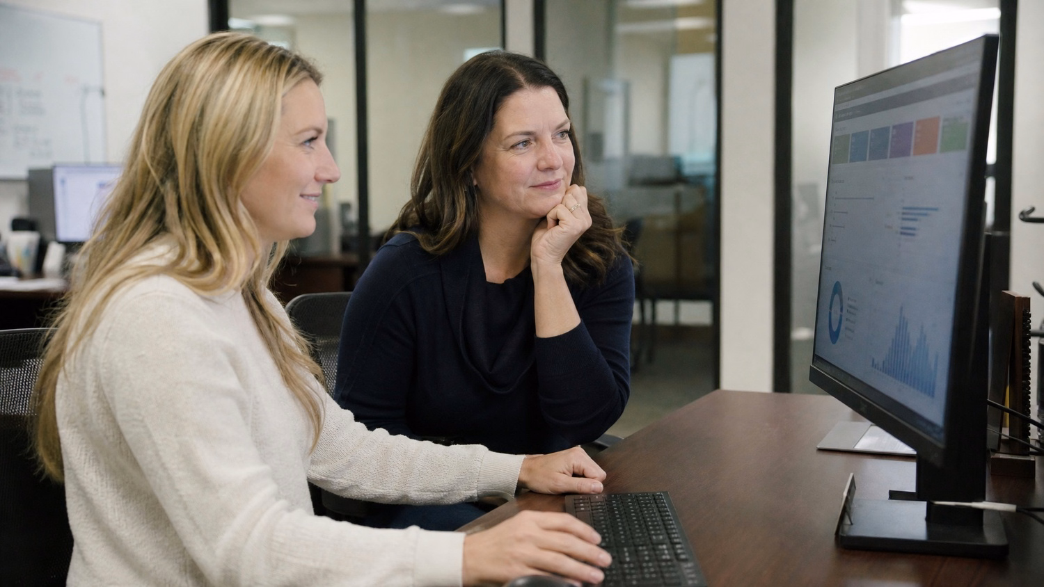 Two women review process dashboard on monitor 60