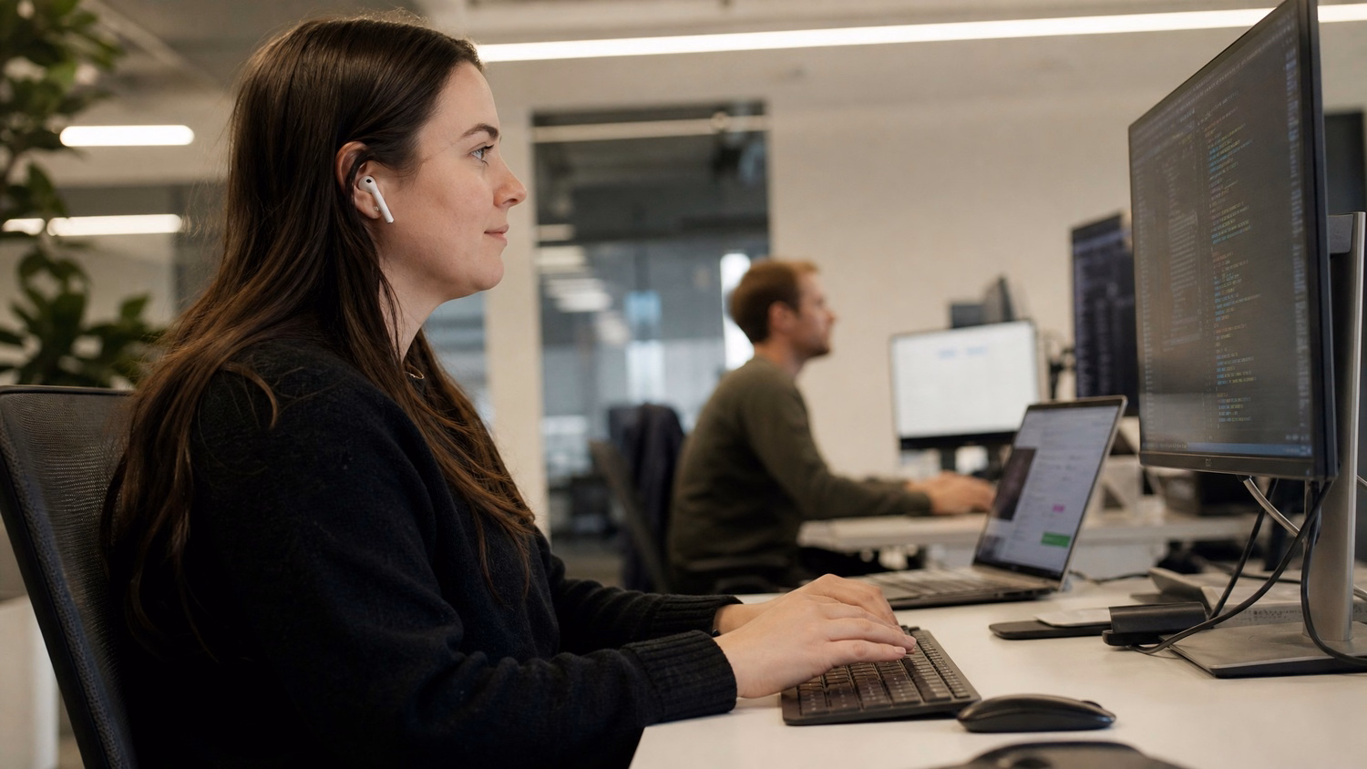 Woman with earbuds coding on a computer screen
