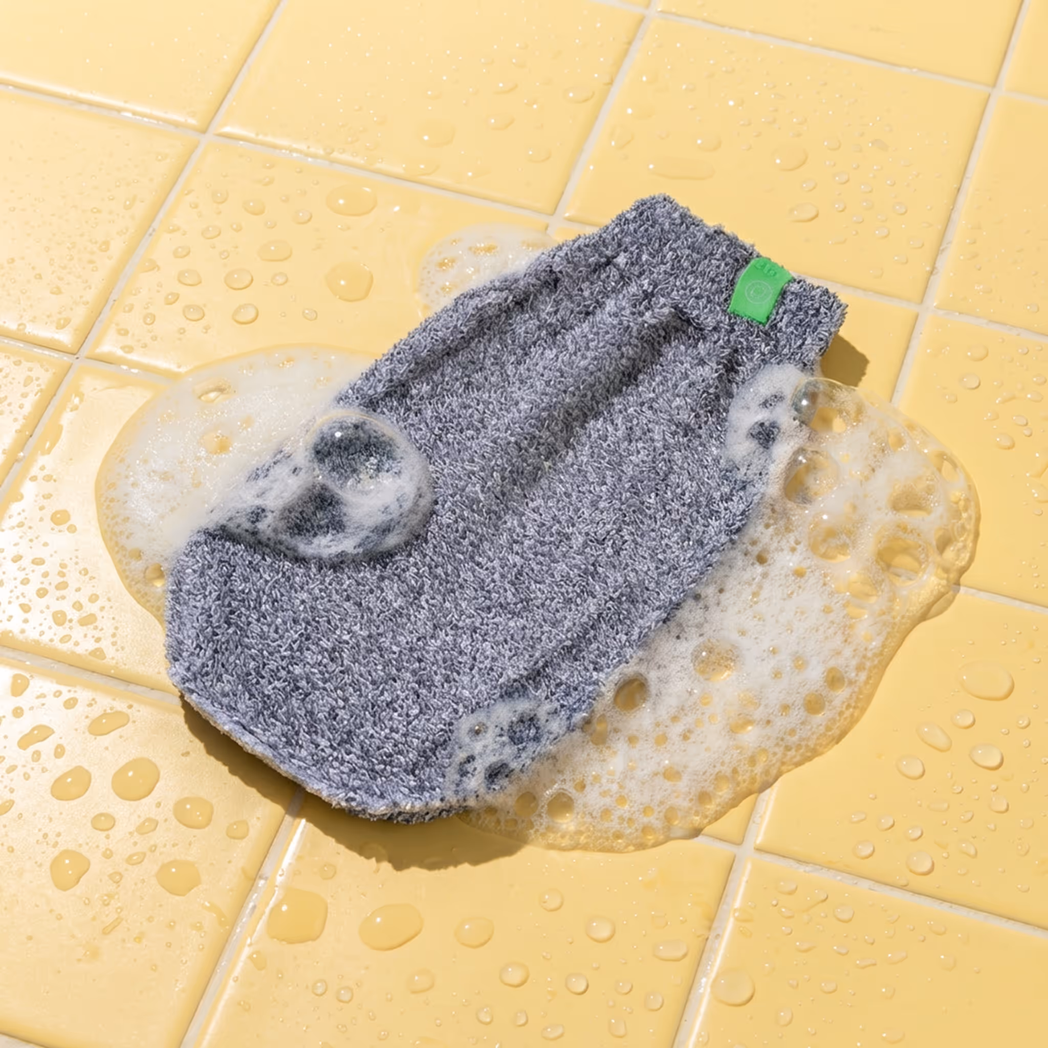 Exfoliating bamboo mitt with foam on wet tile surface