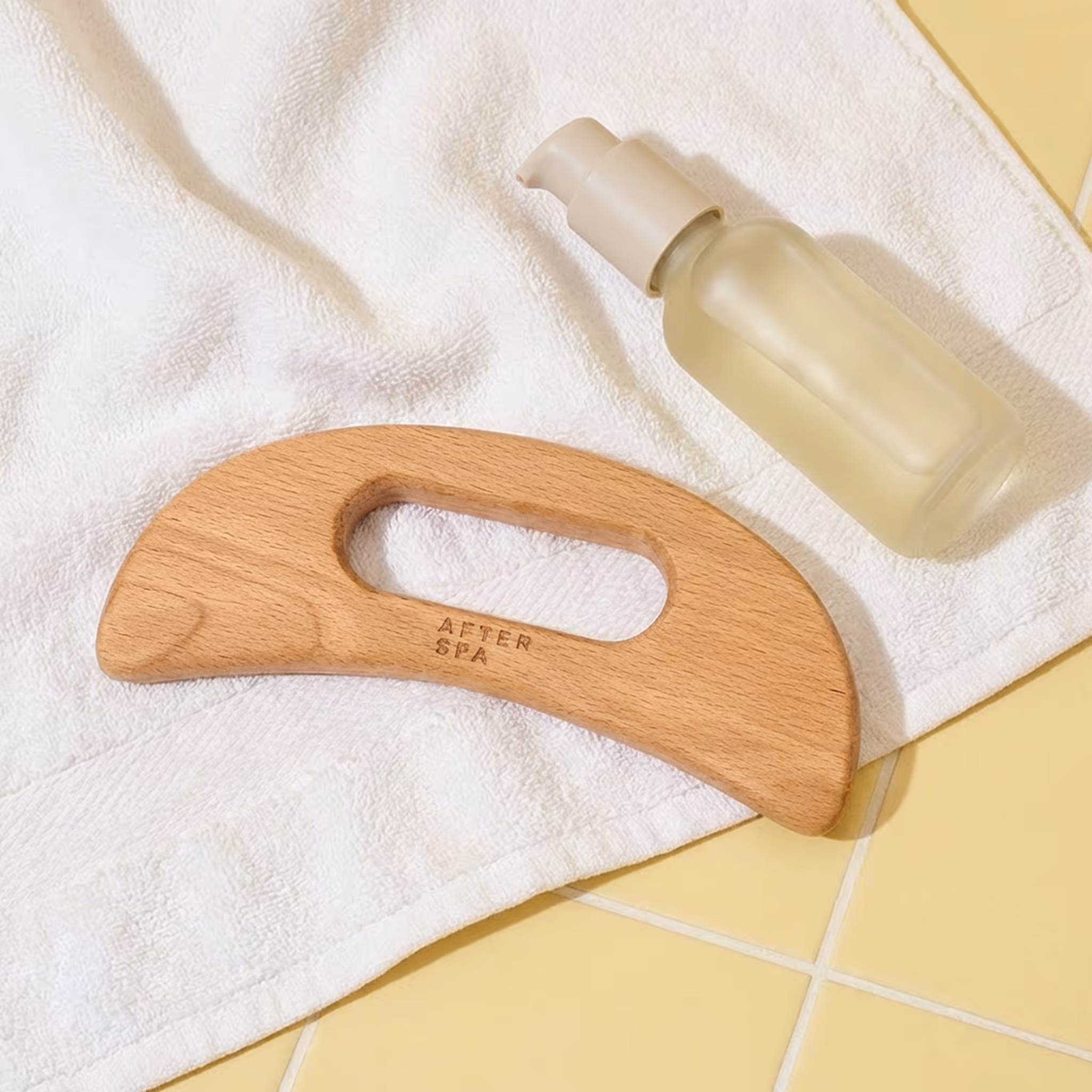 Wooden body gua sha massage tool on white towel beside body oil bottle