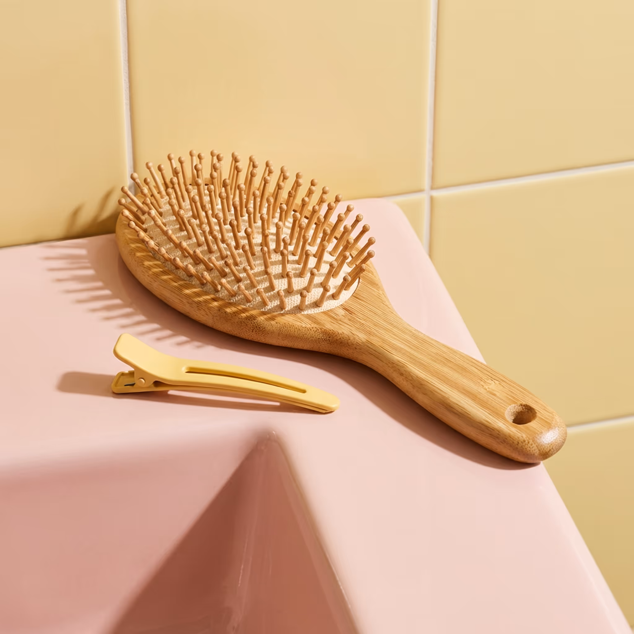 Wooden paddle hair brush resting on pink sink with yellow hair clip