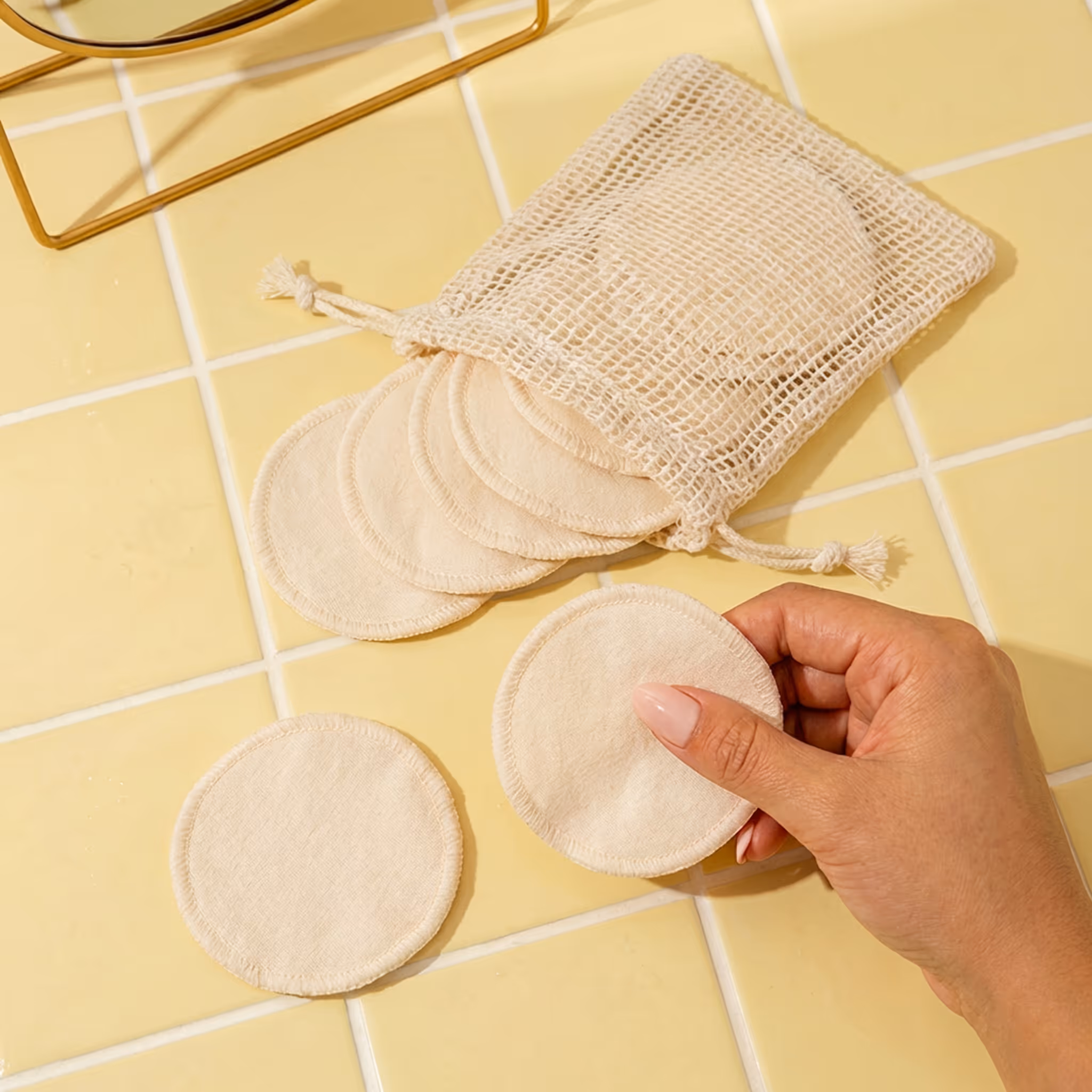 Reusable cotton makeup remover pads with mesh wash bag on yellow tile surface