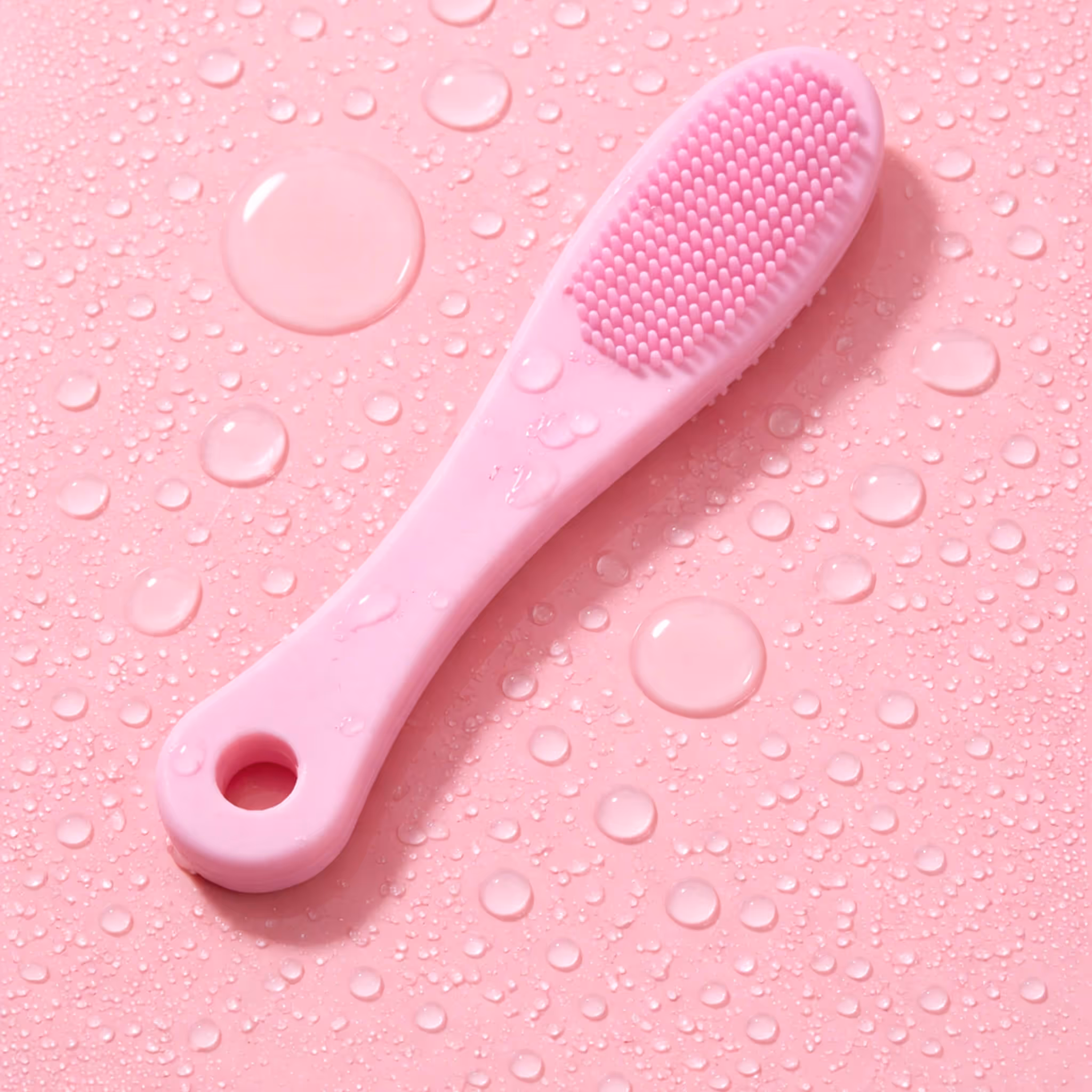 Pink silicone lip scrubber tool with water droplets on pink surface