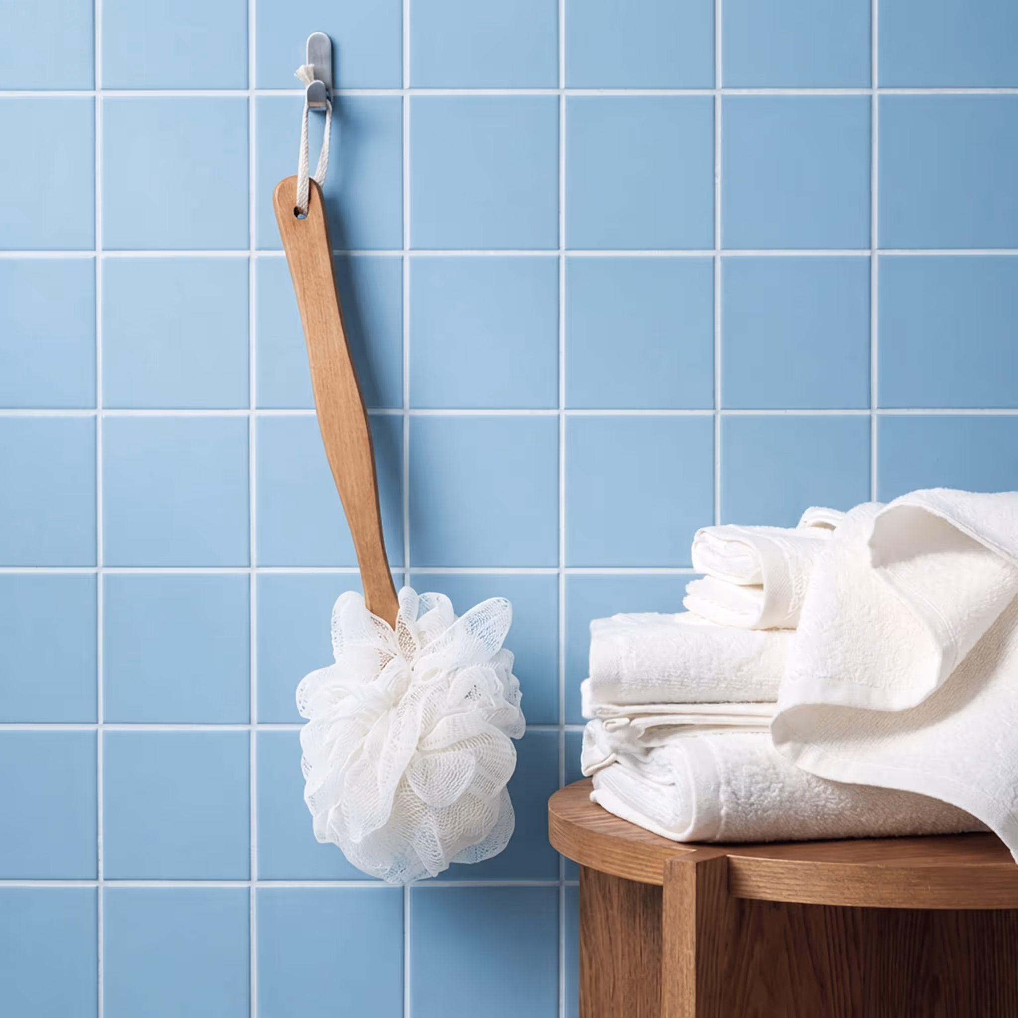 After Spa bath sponge with wooden handle hanging on blue tiled wall beside folded white towels.