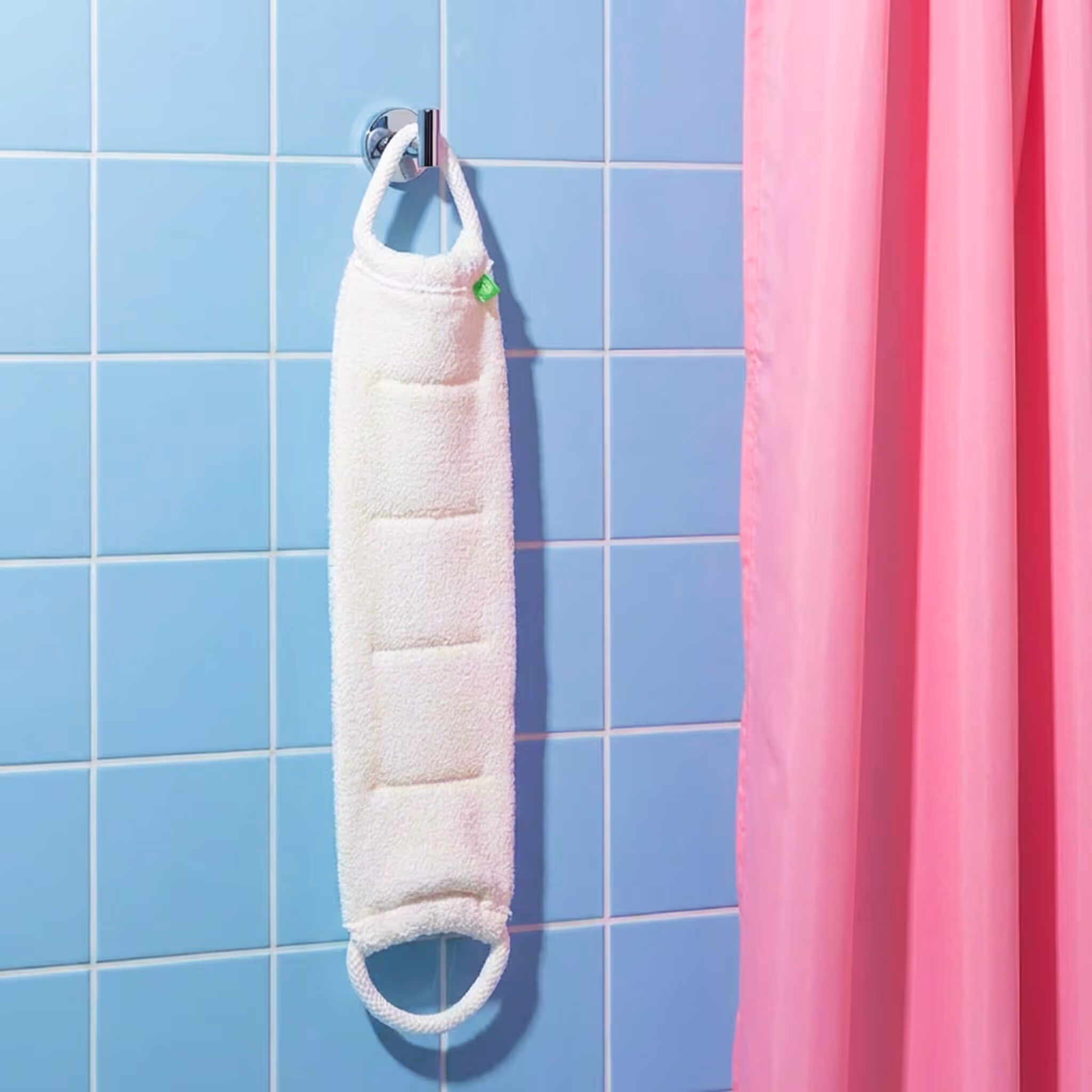 After Spa Back Scrubber hanging on bathroom hook beside blue tile wall and pink shower curtain.