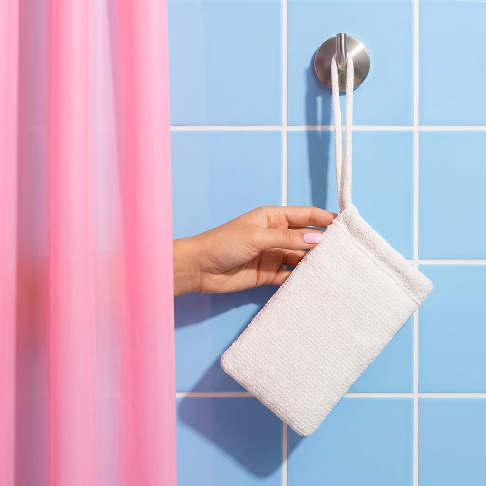 After Spa Body Scrubber hanging from hook in shower with blue tile wall and pink curtain.