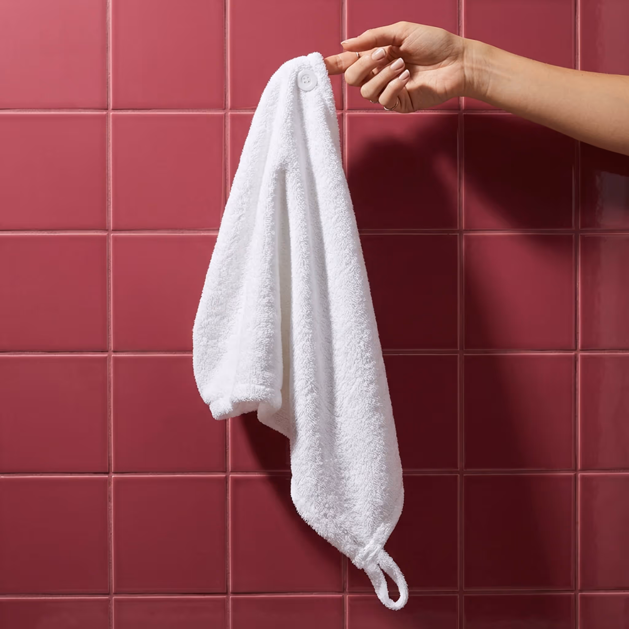 White microfiber hair towel wrap hanging against glossy pink tile wall.