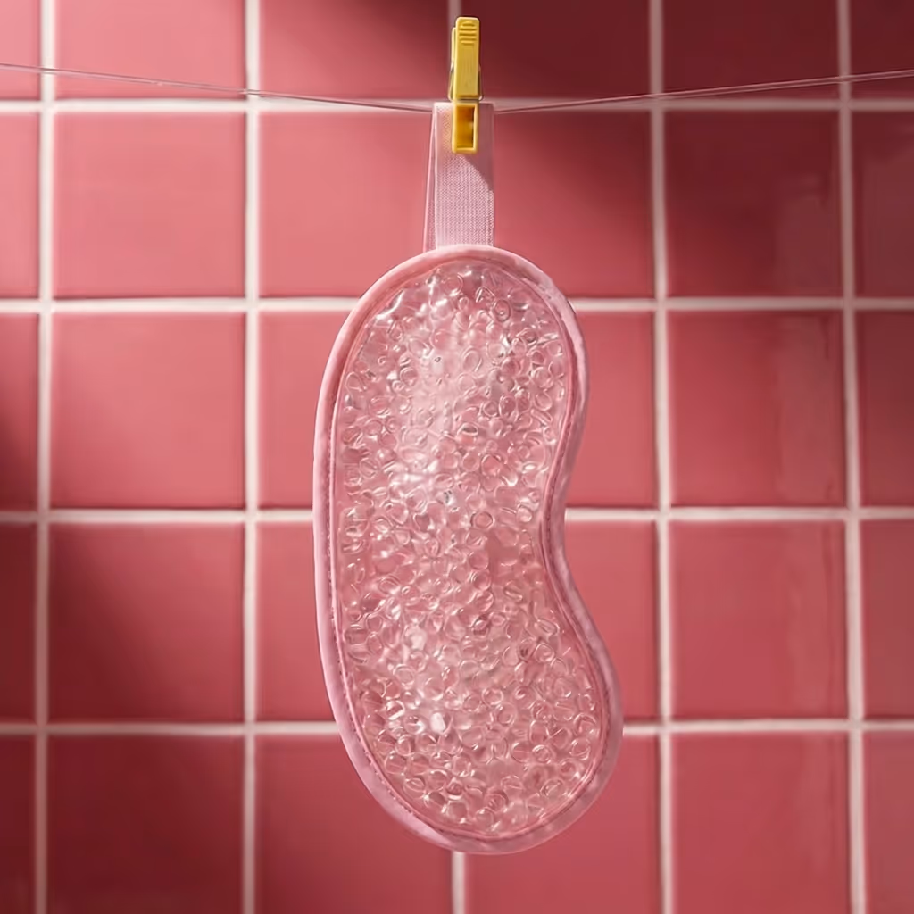 Pink After Spa Eye Gel Mask hanging to dry against glossy pink tile wall.