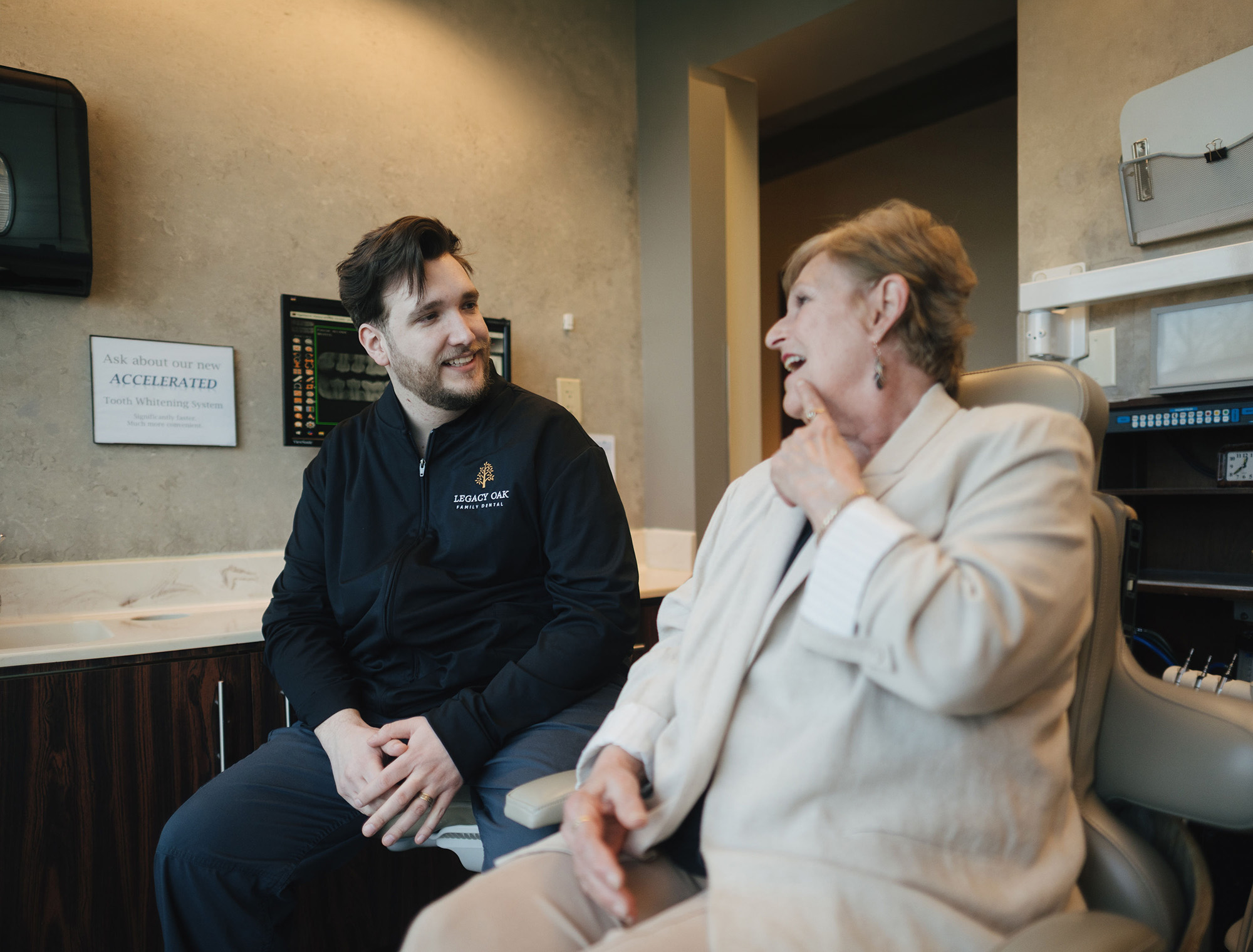 Dental professional in Legacy Oak jacket talking with a smiling elderly woman at the dental office.