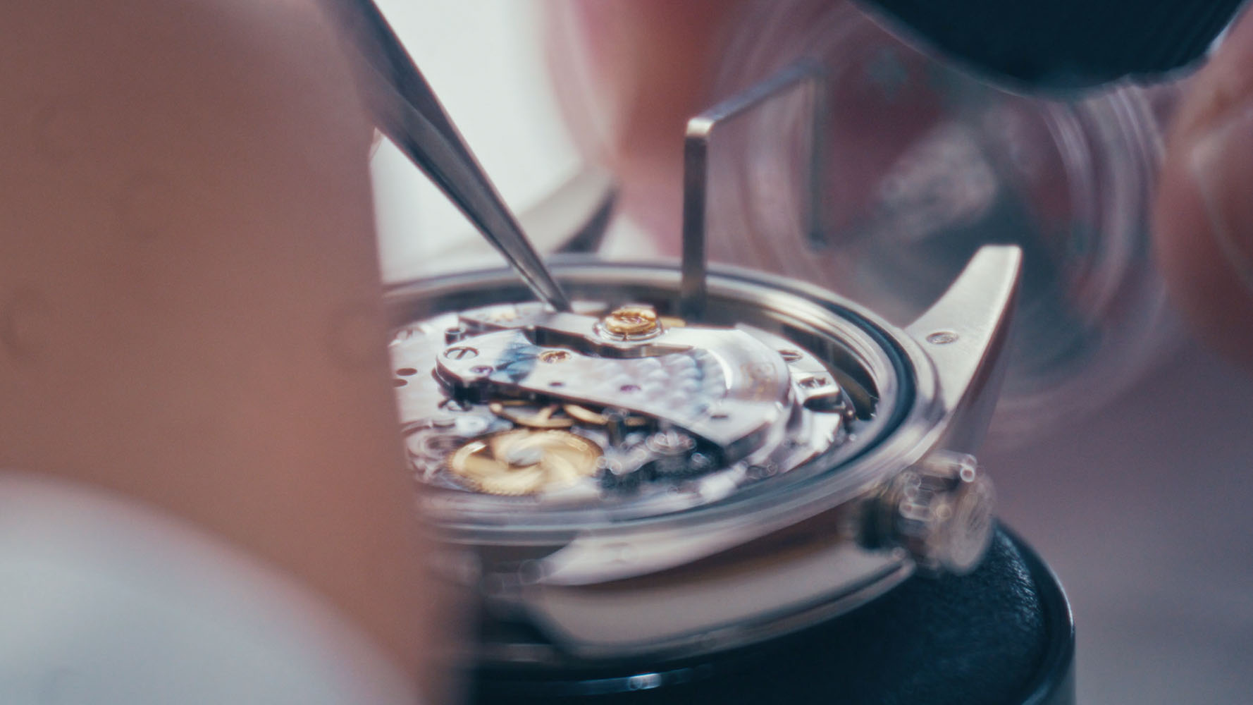 Close-up of hands repairing a mechanical watch movement with tweezers.