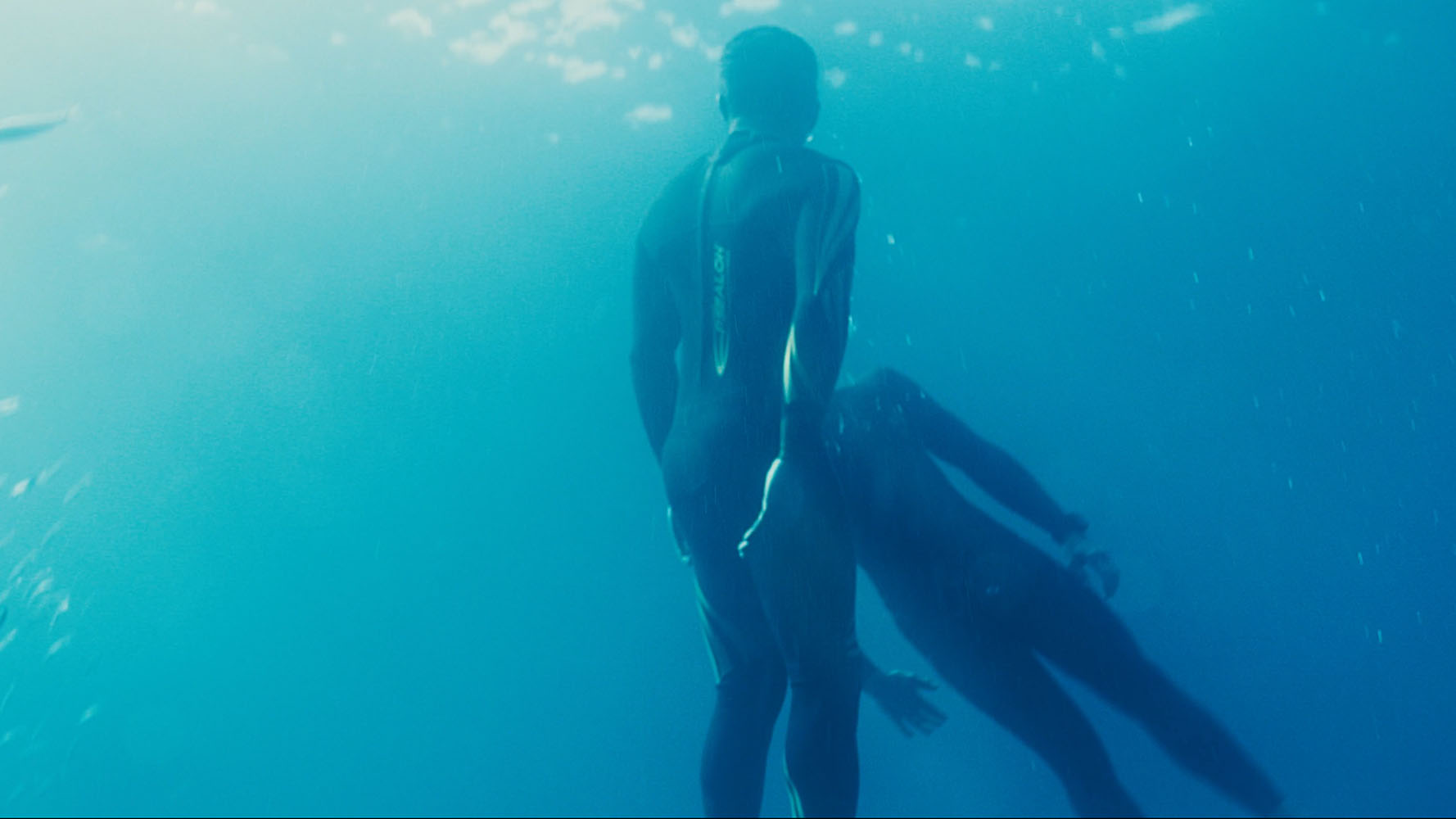Two divers in wetsuits underwater surrounded by blue water and bubbles.