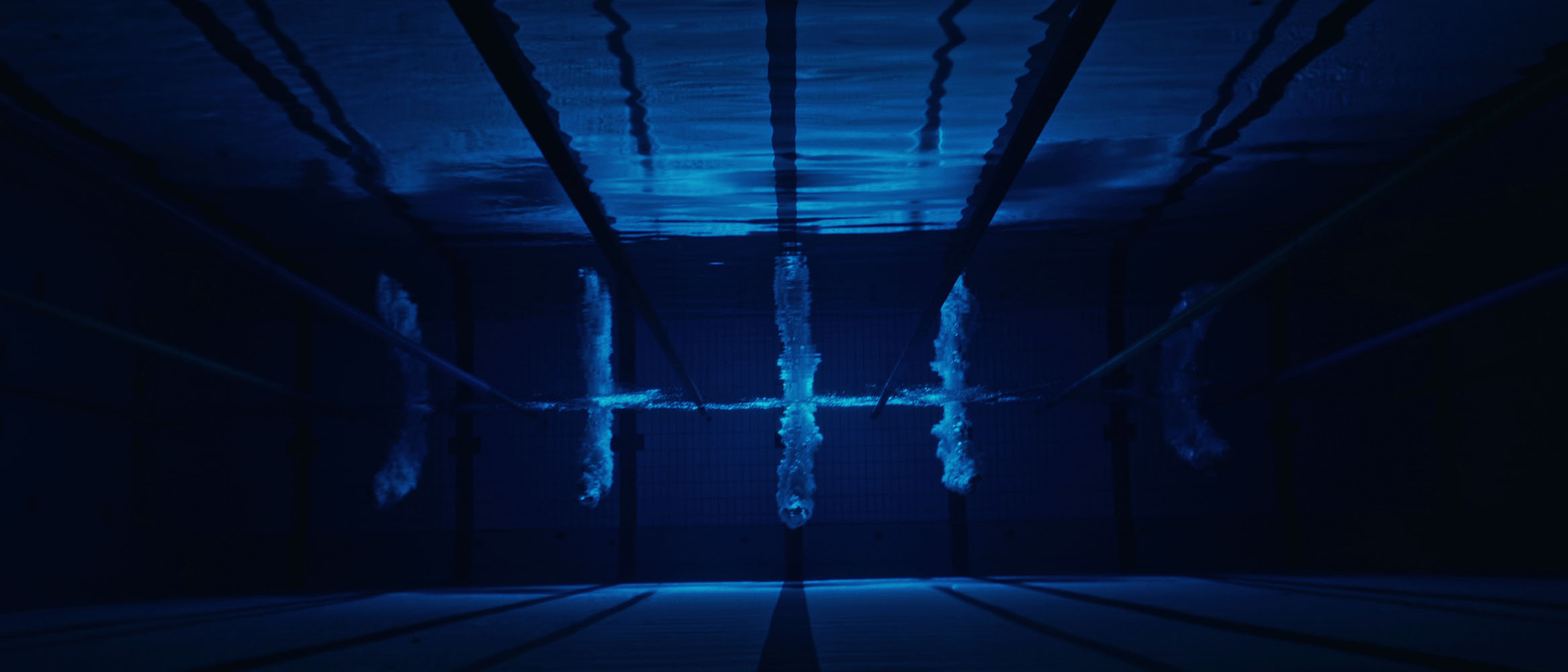 Underwater view of five lanes in a swimming pool with bubbles rising after divers entered the water.