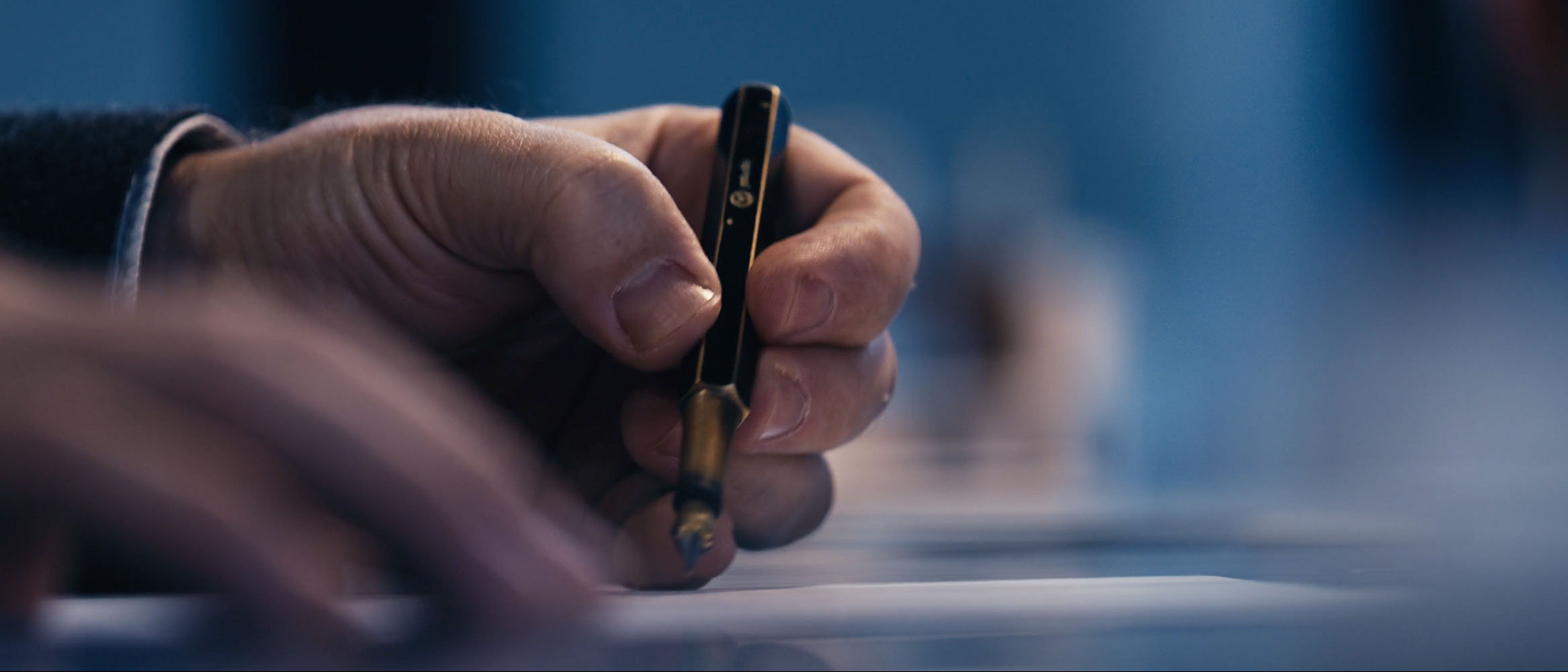 Close-up of a hand holding a fountain pen poised above paper for writing.