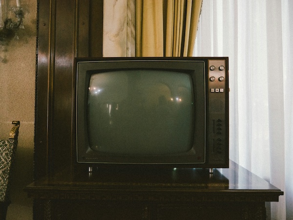 Vintage CRT television with knobs on wooden cabinet in a room with curtains.