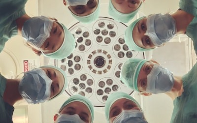 Team of clinicians in surgical caps and masks looking down over a patient