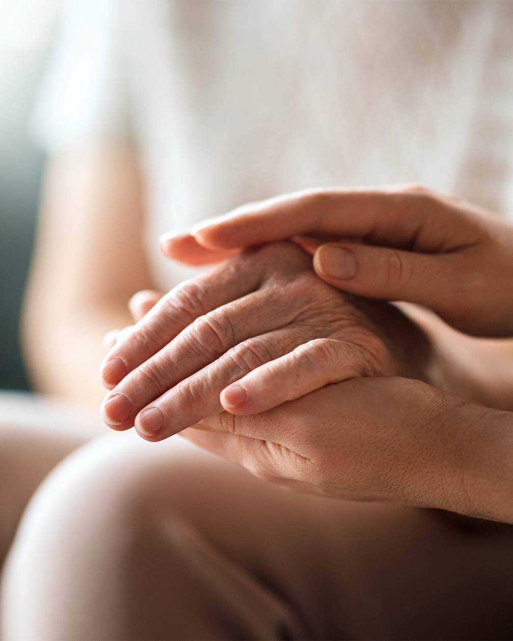 Jüngere Hände halten sanft eine ältere Hand als Zeichen von Fürsorge und Unterstützung.