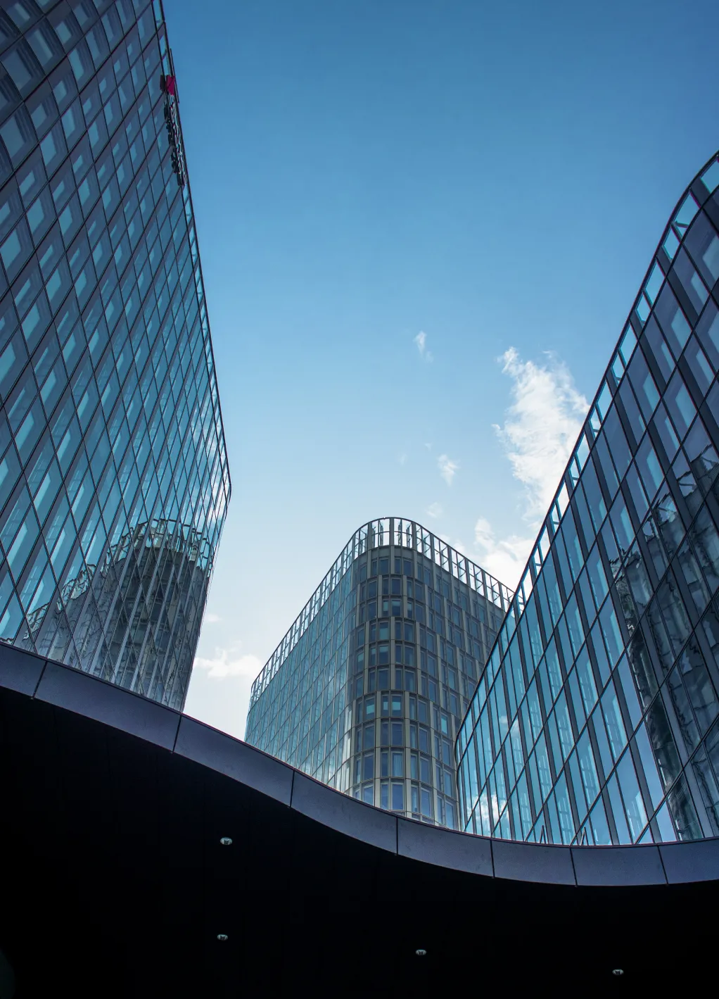 Modern glass skyscrapers viewed from below against a clear blue sky.