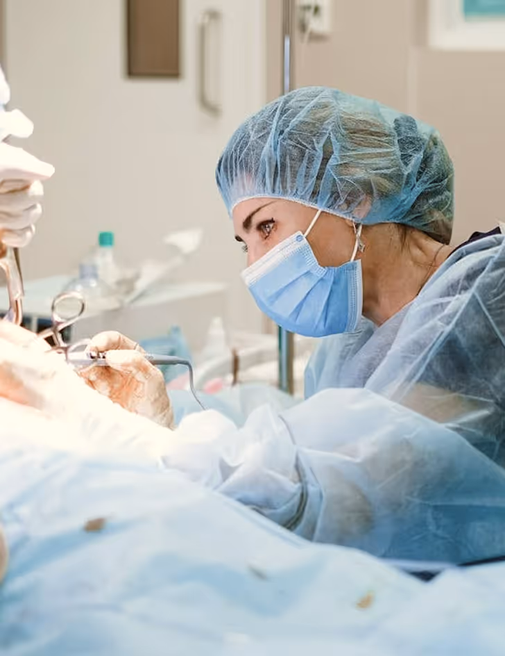 Female surgeon wearing surgical mask and hair cover performing a medical procedure in an operating room.