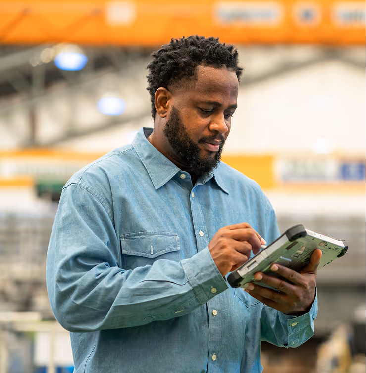 Man in a blue shirt using a handheld device in a warehouse or industrial setting.