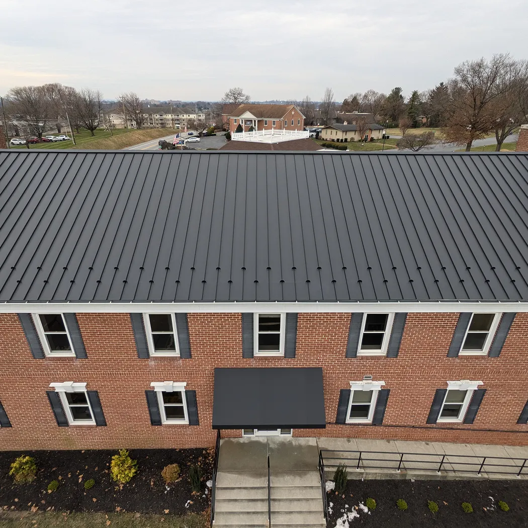Two-story brick building with black shutters and a black metal roof, with a black awning above the entrance stairs.