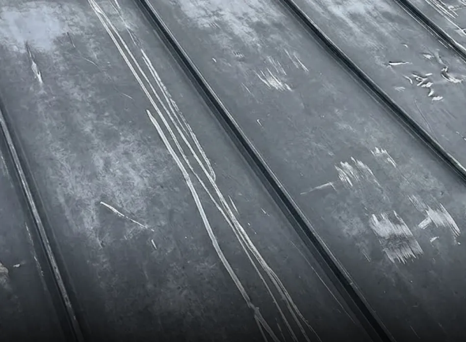 Close-up of a scratched and weathered metal surface with parallel ridges.