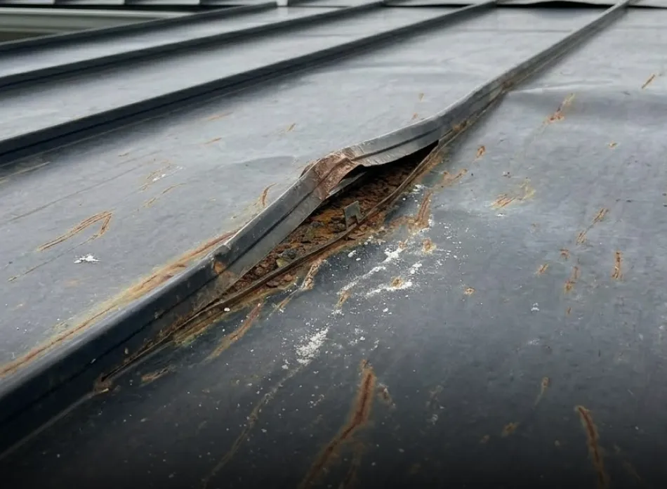 Close-up of a damaged metal surface with a bent and rusted seam and scratches.