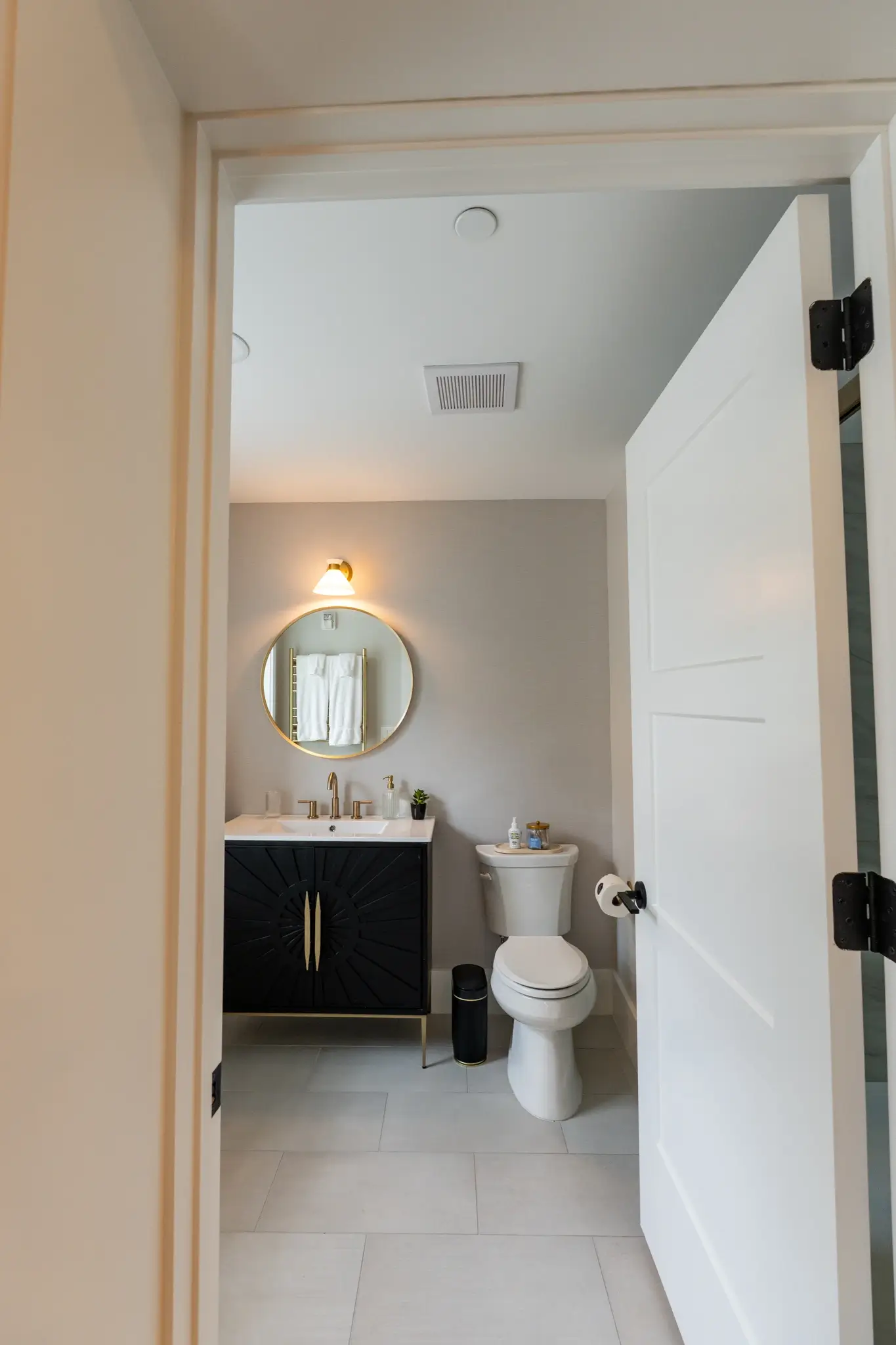 Bathroom entrance showing a dark vanity and round gold-framed mirror in the Landmarks suite at West 22nd Place.