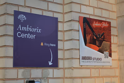 Brick wall with two signs: one for Ambiorix Center instructing to ring a bell, and another for Ambiorix Studio featuring a DJ setup with red lighting.