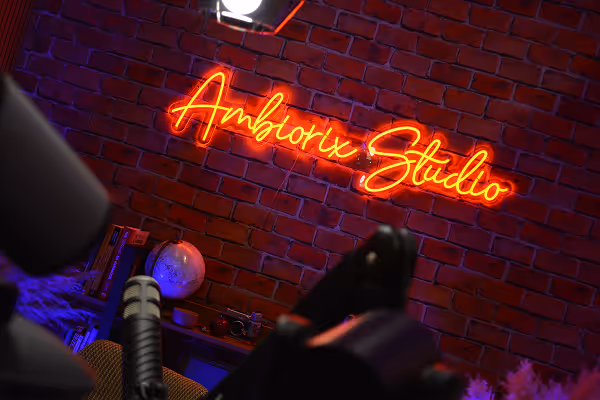 Neon orange sign reading 'Amborix Studio' on a red brick wall with a globe and microphone in the foreground.