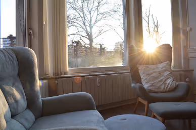 Cozy living room with armchairs and ottoman near a large window with sunlight shining through.