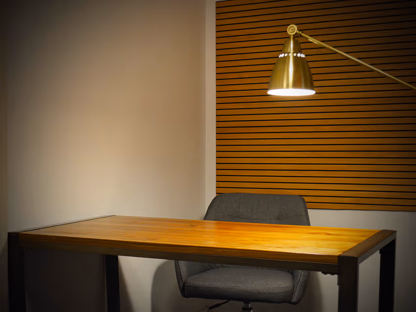 Empty modern wooden desk with a gray office chair and a gold adjustable desk lamp on a wooden slatted wall background.