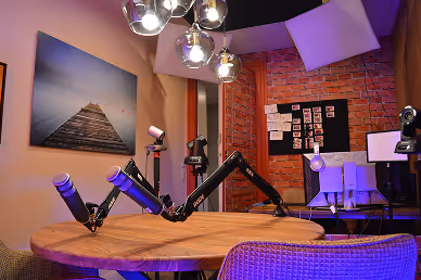 Podcast studio with round wooden table, two microphones on adjustable arms, and ambient lighting.