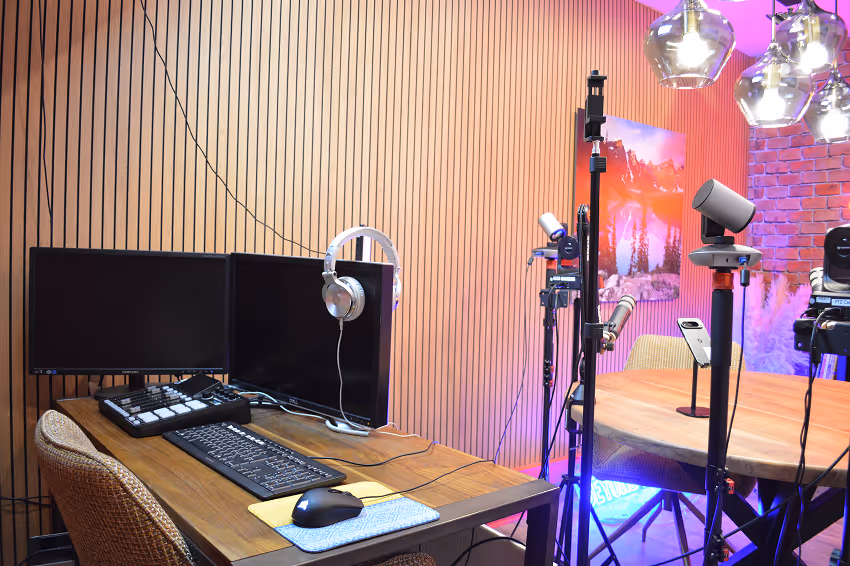 Workspace with a desktop monitor showing a night sky with stars and a green tent, a keyboard, mouse, and microphone on a wooden desk.