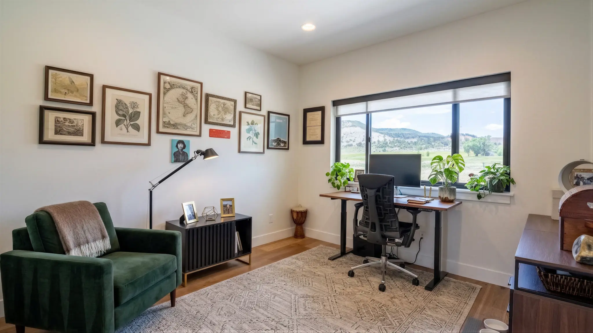 Powder Run home office with green velvet armchair, standing desk with monitor, gallery wall of framed prints, and large window overlooking a green valley
