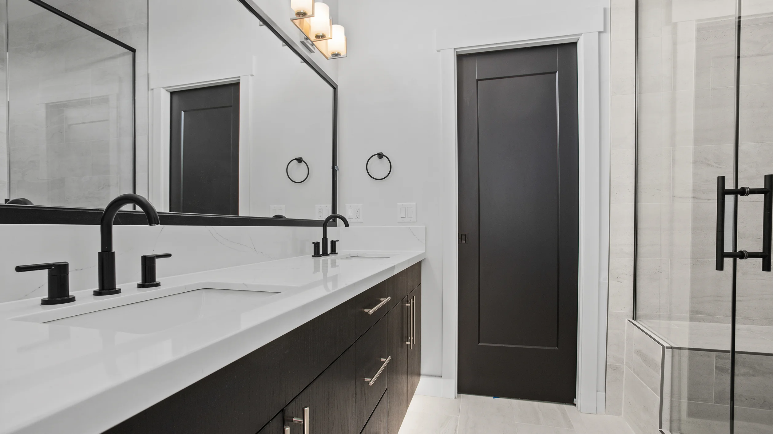 Sunlight bathroom with dark espresso double vanity, white quartz countertop, matte black fixtures, large mirror, and glass walk-in shower with tile
