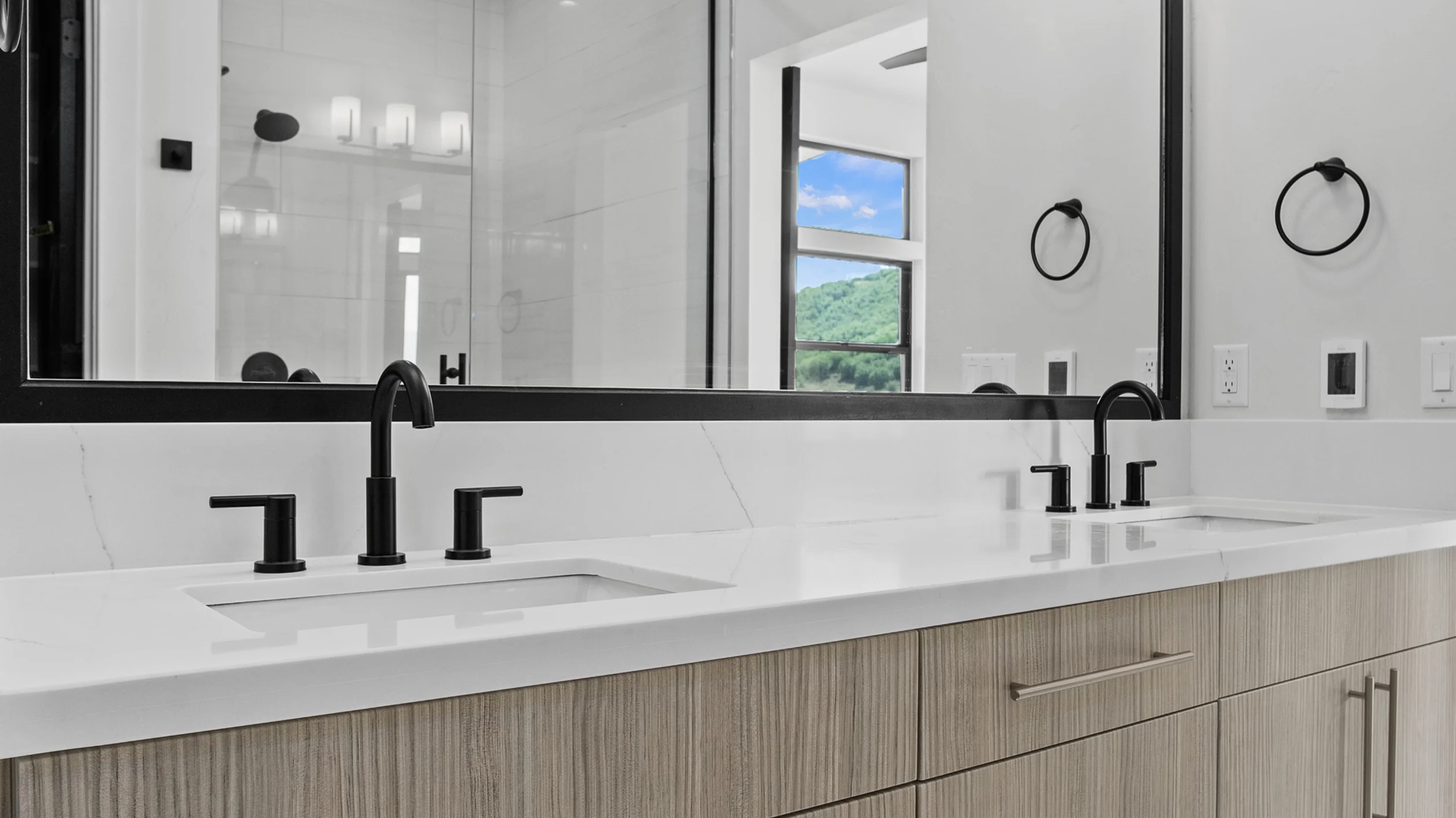 Sunlight primary bathroom vanity closeup with double undermount sinks, white quartz surface, matte black faucets, wide mirror, and mountain views reflected