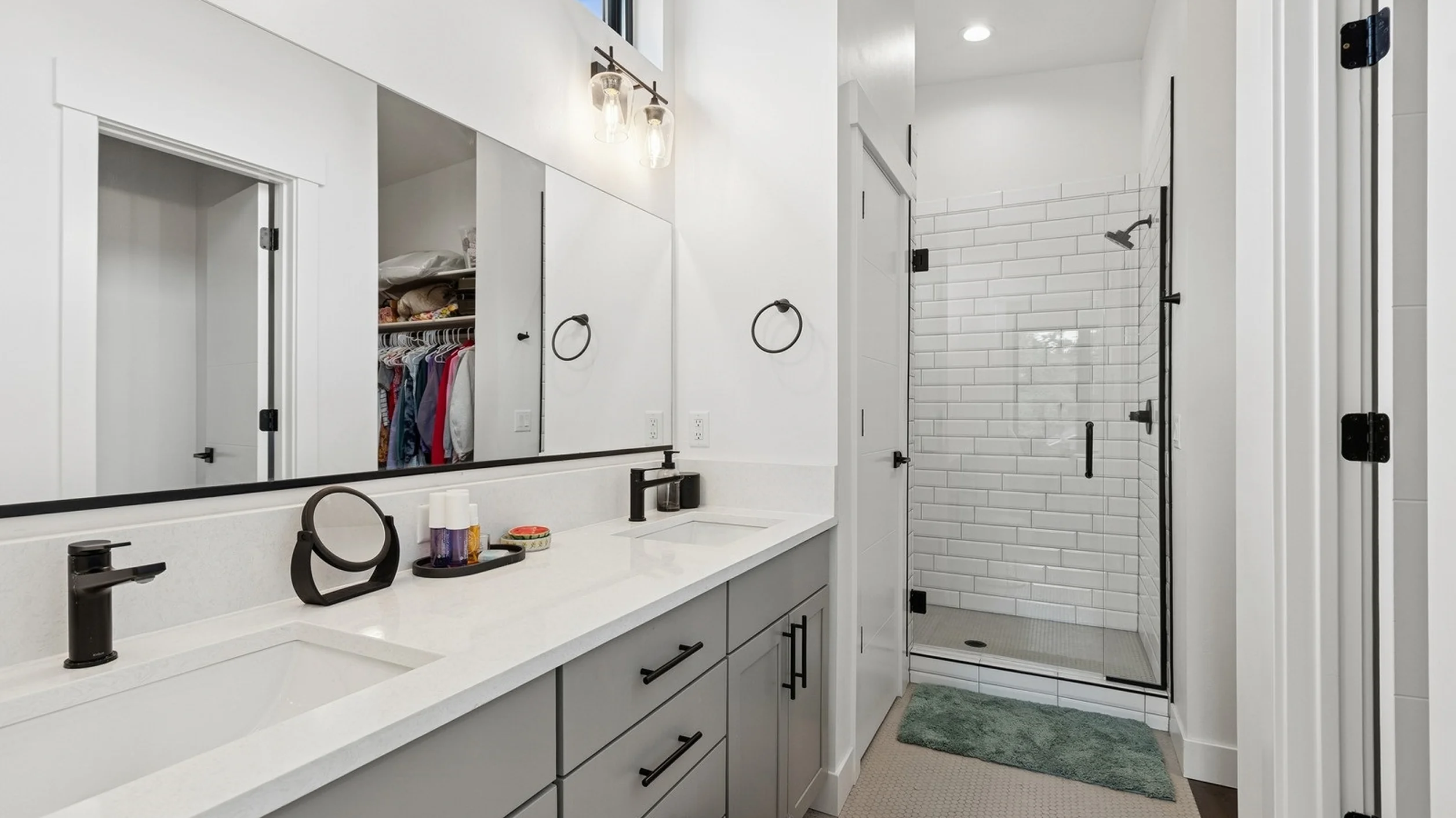 Skyview primary bathroom with double white quartz vanity, matte black fixtures, and glass walk-in shower with white subway tile, mirror reflecting walk-in closet