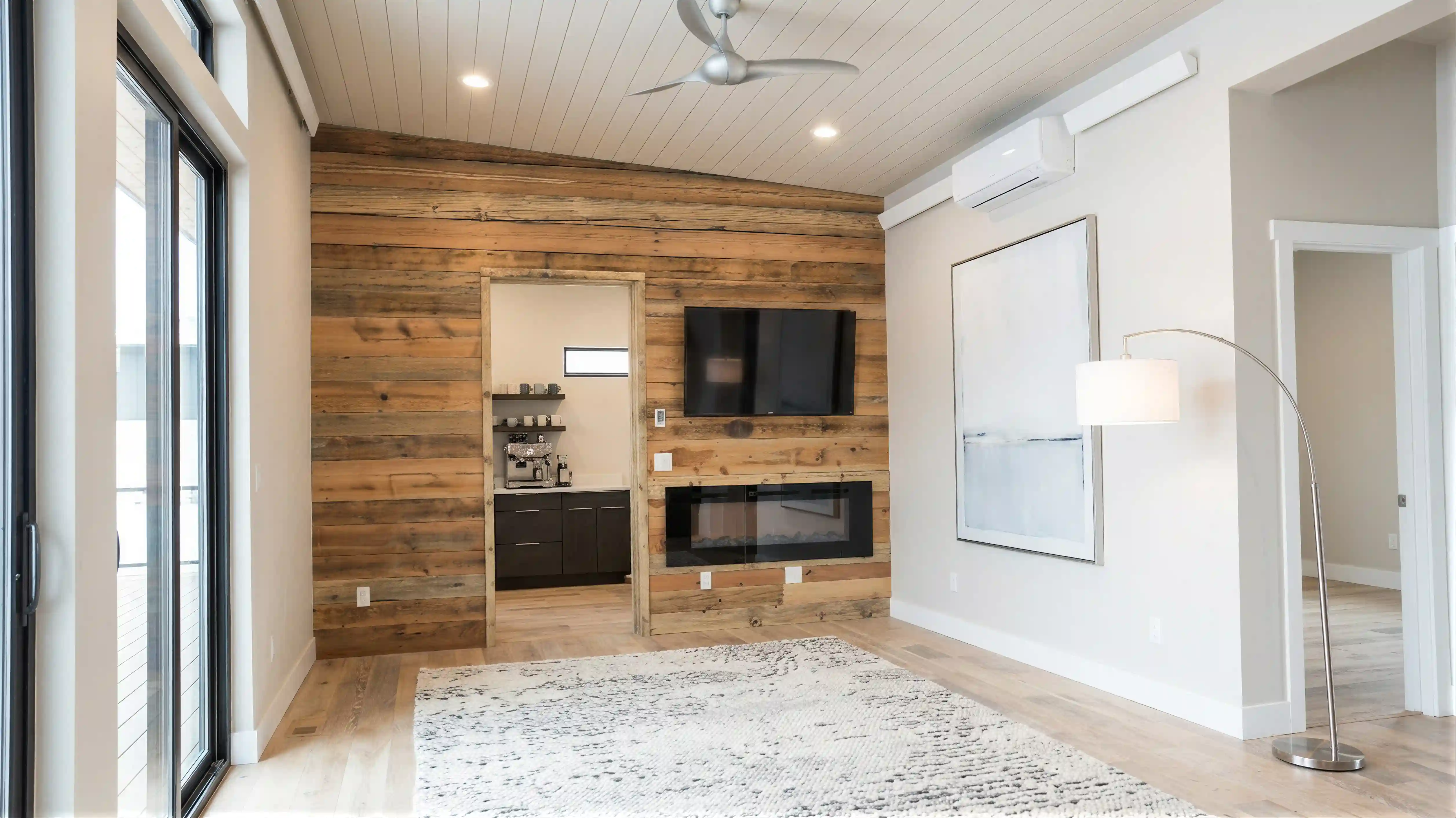 Snow Trace living room with reclaimed wood shiplap accent wall, linear fireplace, wall-mounted TV, white plank ceiling, and sliding glass doors to exterior
