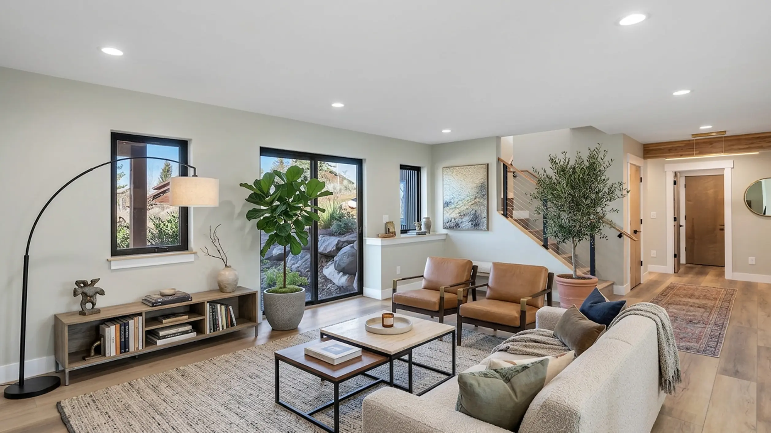 Telemark living room with gray sofa, brown leather chairs, low coffee table, fiddle-leaf fig, hardwood floors, and wood staircase railing