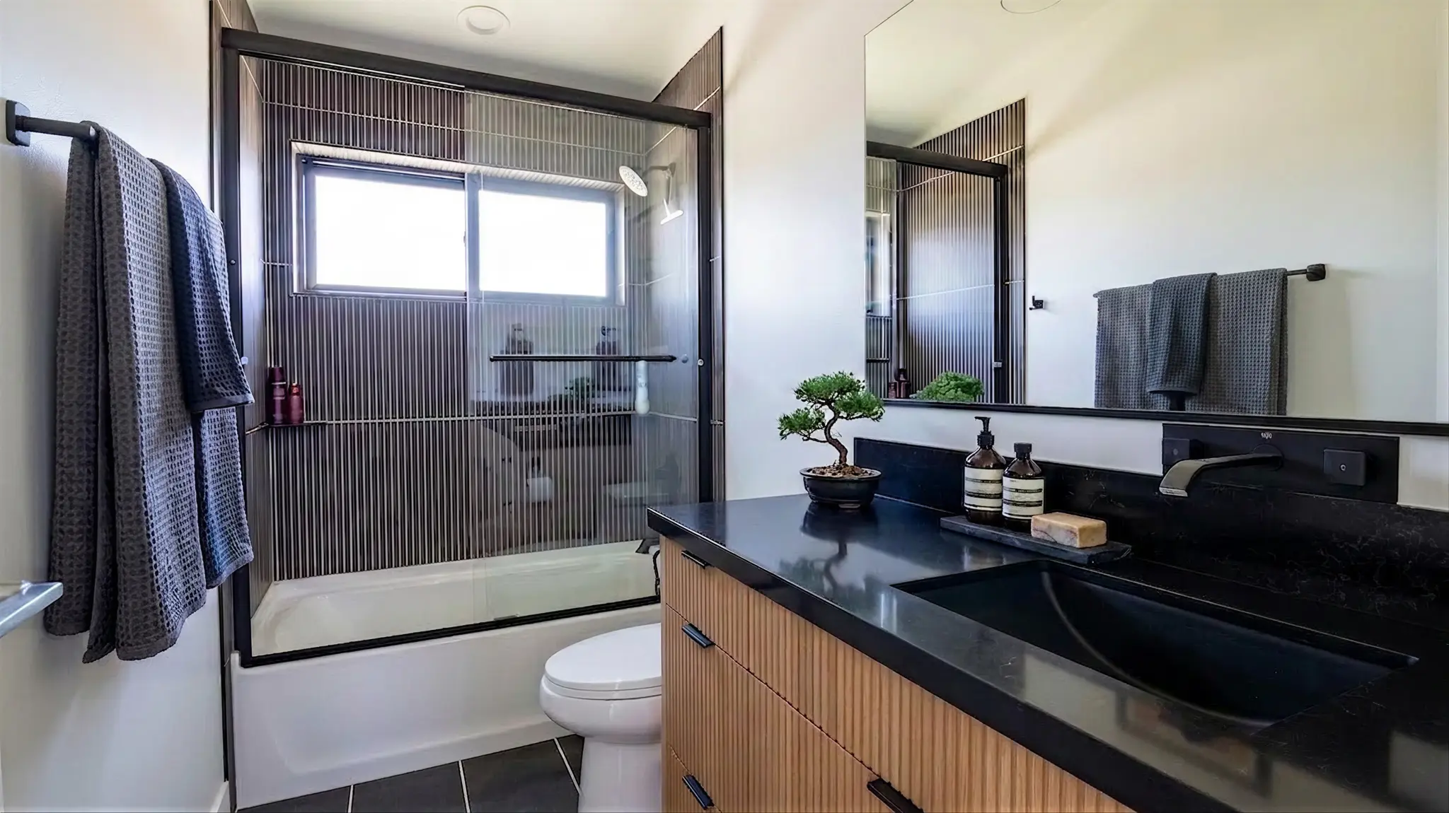 Powder Run bathroom with black quartz countertop, fluted wood vanity, vessel sink, and tub-shower combo with vertical black tile and glass door