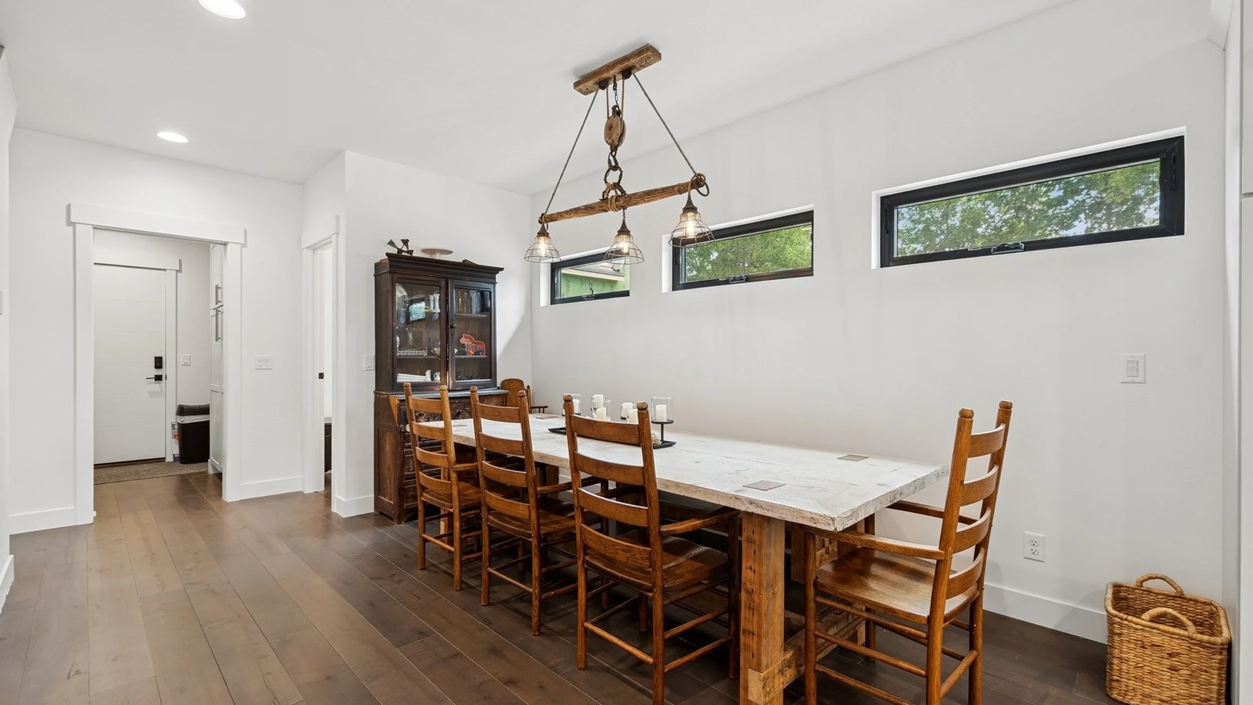 Skyview dining room with long farm table, ladder-back chairs, rustic pulley pendant light, clerestory windows, and dark hardwood floors