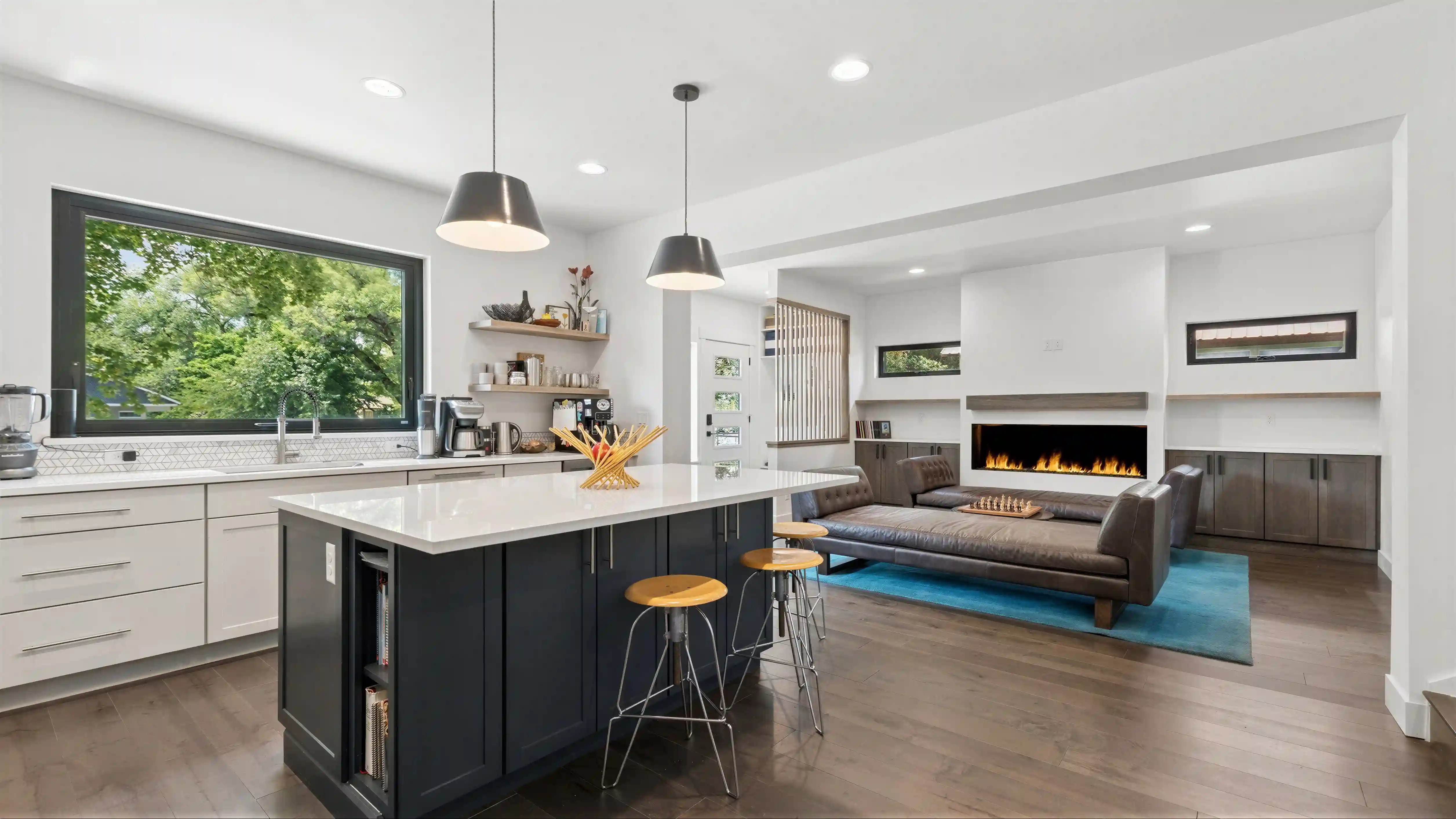 Skyview open-plan kitchen with dark navy island, industrial pendant lights, white cabinetry, and great room with linear fireplace visible beyond