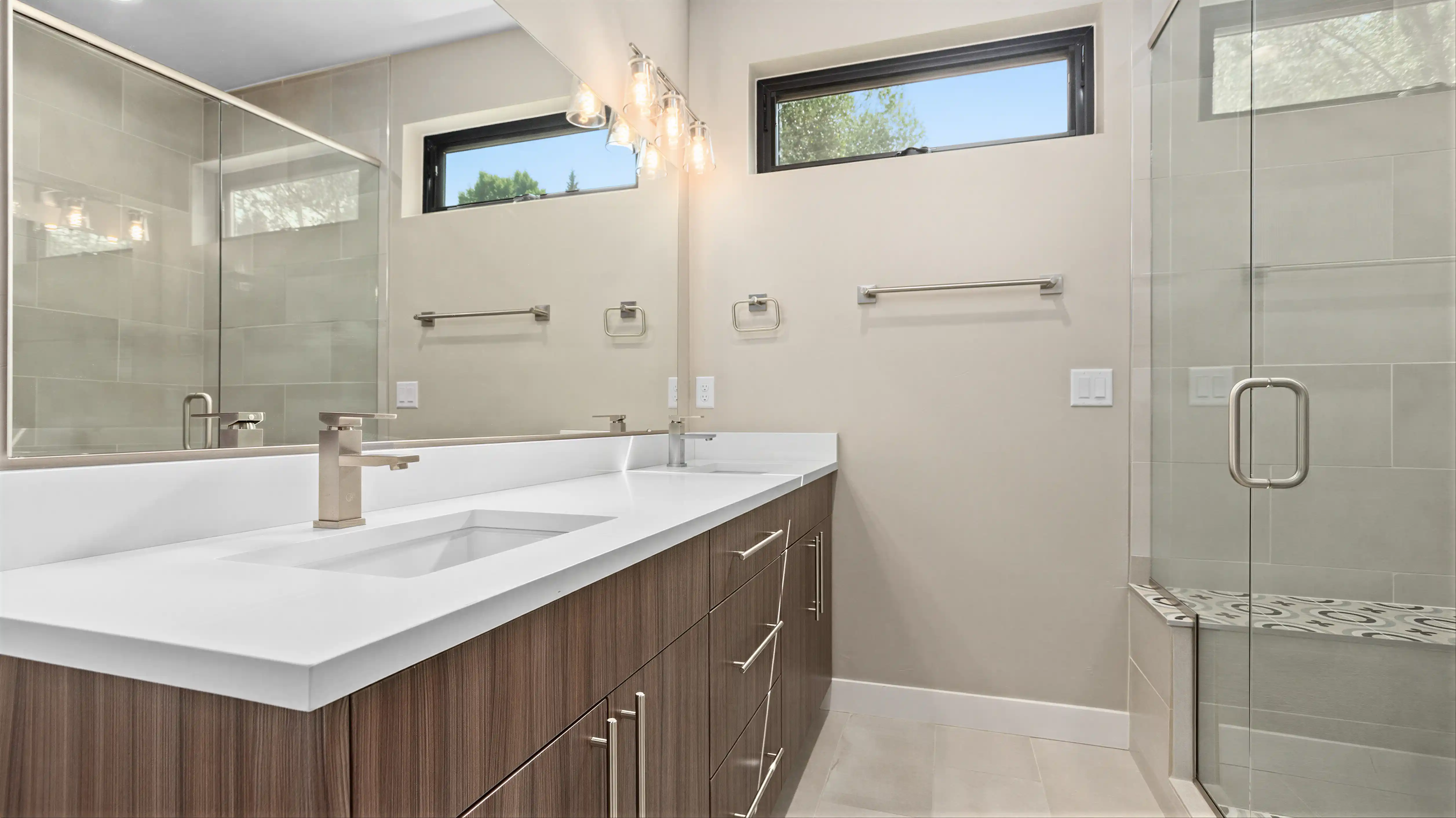High Noon primary bathroom with double white quartz vanity, wood cabinetry, brushed nickel fixtures, and glass walk-in shower with large-format tile