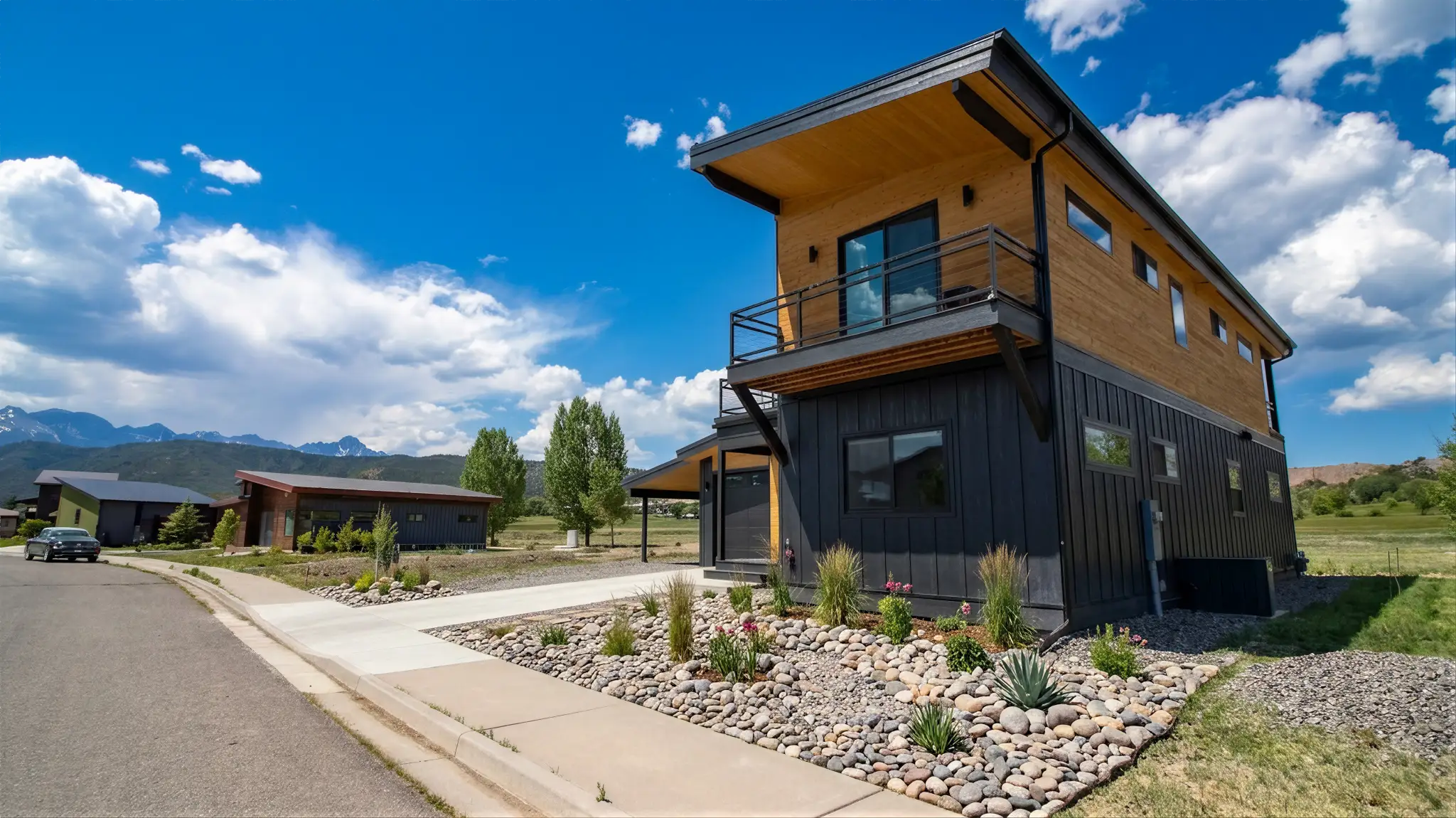 Powder Run exterior showing two-story home with black vertical board-and-batten lower level, warm wood upper story, upper balcony, and mountain valley backdrop